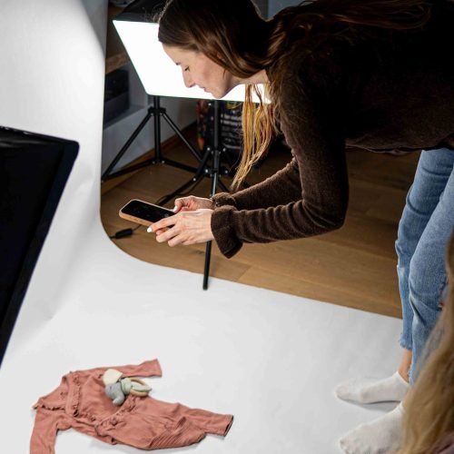 Frau fotografiert Kinderkleidung mit weißem Hintergrund und professionellen Lampen
