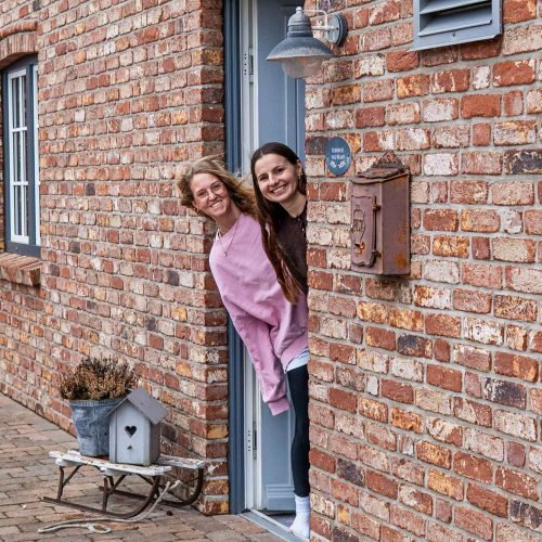 2 Frauen gucken aus Tür von Backsteinhaus